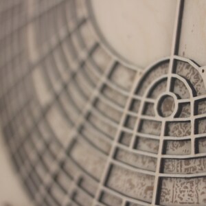 May include: Close-up of a detailed, geometric design with a circular pattern. The design features a series of interconnected lines and shapes, creating a complex, architectural aesthetic. The colour palette is neutral, with shades of grey and beige.