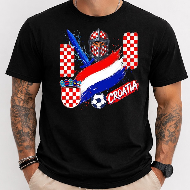 May include: A black t-shirt featuring a graphic design with a knight in a red and white checkered helmet, a blue sword, a soccer ball, the Croatian coat of arms, a red, white, and blue brushstroke flag, and the text CROATIA in red letters.