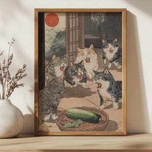 Op de afbeelding: Een vintage Japanse houtsnede die vijf katten laat zien die naar een komkommer op een bord kijken. De katten staan in verschillende poses, sommige met hun mond open alsof ze miauwen. De print is ingelijst in een houten lijst.