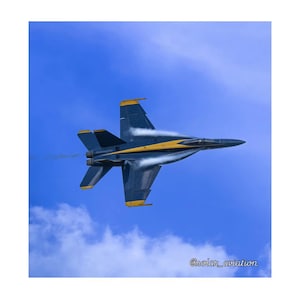 Puede incluir: Un avión de combate azul y amarillo vuela por un cielo azul claro, dejando un rastro de humo blanco detrás. El avión está en un giro pronunciado, con las alas inclinadas hacia arriba. El cielo es de un azul brillante, con algunas nubes blancas en la distancia. La imagen se toma desde abajo del avión, mirando hacia arriba.