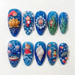 May include: A set of ten blue acrylic nails with ocean-themed designs. Each nail features a different miniature ocean scene, including fish, sea creatures, and characters. The designs are detailed and colorful, with a glossy finish.