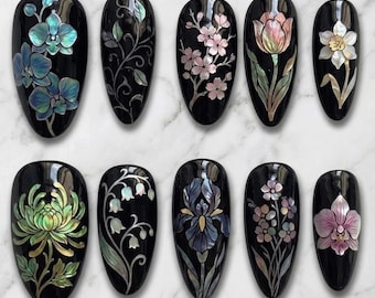 Könnte beinhalten: Zehn schwarze Nageldesigns mit floralen Mustern. Jeder Nagel zeigt eine andere Blume, darunter Orchideen, Kirschblüten, Tulpen und Iris, mit schillernden Akzenten. Die Designs sind vor einem Marmorhintergrund angeordnet.