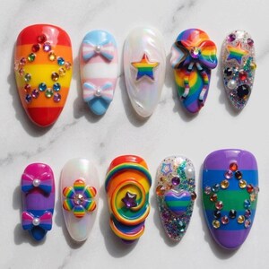 May include: A set of ten press-on nails featuring vibrant rainbow stripes, iridescent finishes, and 3D embellishments including colorful rhinestones, bows, stars, hearts, and flowers. Each nail displays a unique design with varied textures.