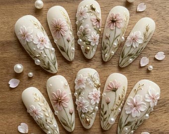 May include: A set of ten almond-shaped artificial nails, each adorned with delicate, three-dimensional floral designs in shades of pink and white. The nails feature pearl accents and gold embellishments, creating an elegant, feminine aesthetic.