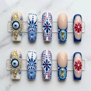 May include: A set of ten press-on nails featuring a variety of designs including a gold-toned evil eye charm with rhinestones, intricate blue and white filigree patterns, and blue-tipped French manicures accented with gold rose charms and red flowers.