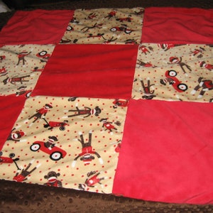 May include: A red and beige patchwork quilt with a pattern of monkeys riding toy cars. The quilt is made of soft, plush fabric and is perfect for a child's room.
