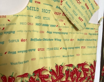 May include: Yellow kitchen apron with red chili peppers and the text "MILD HOT" and "SUPER HOT" printed on it. The apron has a matching pot holder with the text "Buffalo Chicken Wing" printed on it.