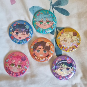 Op de afbeelding: Vijf ronde buttons met gestileerde anime-karaktergezichten en holografische accenten. De buttons zijn voorzien van de namen Ivan, Till, Luka, Hyuna, Mizi en Sua, elk omringd door kleurrijke hartjes en stervormige grafische elementen.