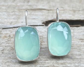 May include: A pair of silver dangle earrings with light blue rectangular gemstones. The earrings have a simple design and are perfect for everyday wear.
