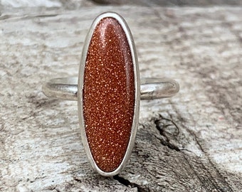 May include: A silver ring with an oval-shaped red sandstone stone.