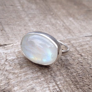 May include: A silver ring with a large oval moonstone. The stone has a milky white color with a hint of blue.