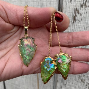 May include: A set of gold-plated arrowhead shaped earrings and a necklace with iridescent green and blue stones.
