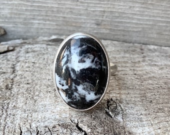 May include: A silver ring with a black and white oval gemstone. The gemstone has a swirling pattern.
