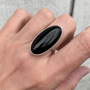 May include: A silver ring with a large, oval-shaped black gemstone.