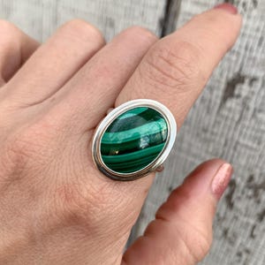 May include: A silver ring with a green malachite oval gemstone set in a bezel setting.