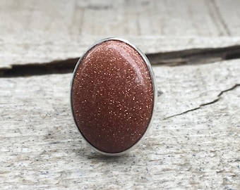May include: A silver ring with a large oval-shaped red sandstone stone.