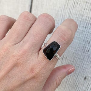 May include: A silver ring with a black rectangular gemstone. The ring has a textured band.