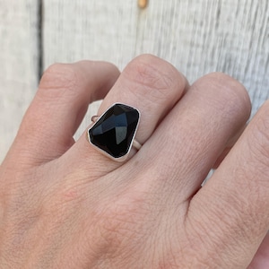 May include: A silver ring with a large, faceted black gemstone. The ring is on a person's finger.