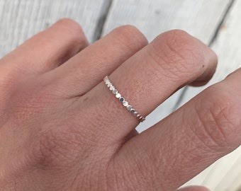 Puede incluir: Un delicado anillo de plata con una fila de pequeñas cuentas redondas.