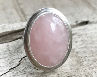 May include: A silver ring with a large oval-shaped pink rose quartz gemstone.