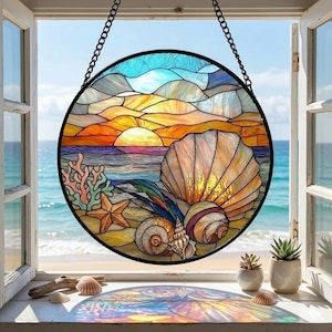 May include: Round stained glass window art depicting a beach scene with a sunset, seashells, and coral. The artwork is framed in black and hangs from a chain. The colors include blues, oranges, yellows, and browns.