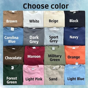 以下が含まれることがあります： 茶色、白、ベージュ、黒、カロライナブルー、ダークグレー、スポーツグレー、ネイビー、チョコレート、マルーン、ミリタリーグリーン、オレンジ、フォレストグリーン、ライトピンク、サンド、ライトブルーなど、さまざまな色のクルーネックのスウェットシャツのグリッド。「Choose color」の文字が上にあります。