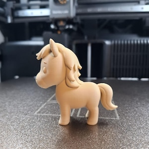 May include: A light tan 3D-printed pony figurine. The pony has a flowing mane and tail, and is standing on a textured surface. The figurine is a cute, stylized representation of a horse.