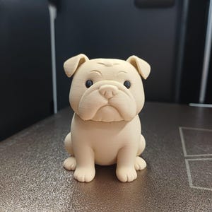 Op de afbeelding: Een beige bulldogbeeldje met een gedetailleerd, getextureerd oppervlak. De bulldog zit rechtop met zijn poten naar voren en heeft zwarte ogen. Het beeldje is een decoratief item, waarschijnlijk 3D-geprint.
