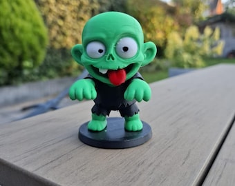 May include: A green zombie figure with a red tongue, white eyes, and black clothing. The figure stands on a black circular base. The zombie has large ears and its arms are outstretched.