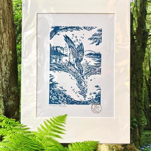 May include: A framed blue and white linocut print showing a bird diving into water. The artwork is titled "Honeycrisp Descent" and includes an artist's signature. The print is matted in white and encased in a clear protective sleeve.