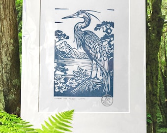 Puede incluir: Una impresión enmarcada en azul y blanco de una garza cerca del agua, con montañas al fondo. La impresión está en un marco y paspartú blancos. El texto "WHERE THE HERON WAITS" está en la parte inferior.