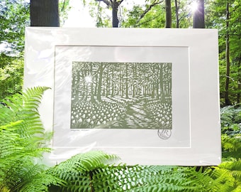 Puede incluir: Una impresión enmarcada que representa un paisaje forestal en tonos verdes y blancos. La obra de arte muestra un camino que serpentea entre los árboles, con un efecto de sol. La impresión está montada en un passe-partout blanco y un marco blanco.