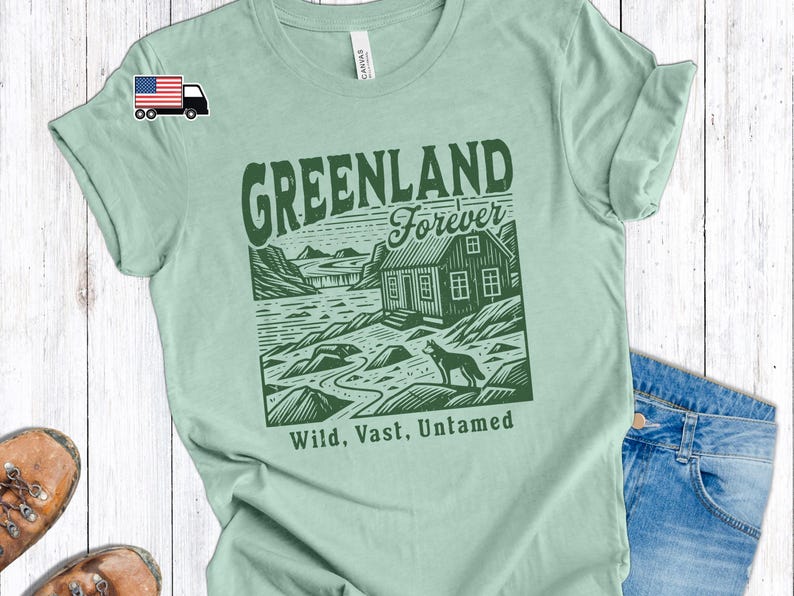 May include: Green t-shirt with a graphic design of a cabin, a wolf, and the text "Greenland Forever" in a vintage style font. The text "Wild, Vast, Untamed" is below the graphic.