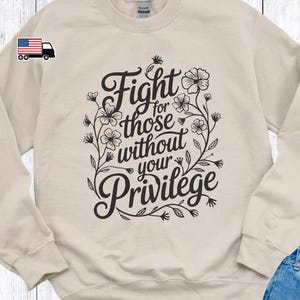 May include: A beige sweatshirt with a black floral design and the text "Fight for those without your privilege".
