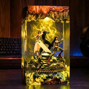 May include: A rectangular resin lamp featuring three miniature figures standing on a rocky base. The central figure holds a large sword, flanked by two other figures. The interior is illuminated with a warm yellow light and swirling smoke effects.