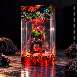 Op de afbeelding: Een rechthoekig blok van hars met een miniatuur krijgersfiguur in groen en metallic pantser. Het interieur bevat wervelende rode en oranje rookeffecten, met een getextureerde, gloeiende rode basis en een donker, gemarmerd bovengedeelte.