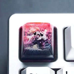 May include: A custom keyboard keycap featuring a koi fish design. The keycap has a clear resin body with a vibrant underwater scene in shades of red, purple, and blue. The koi fish is white with black markings.