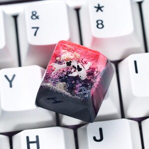 May include: A custom keyboard keycap featuring a koi fish design. The keycap is a mix of red, pink, black, and white. The koi fish is white with black spots, and the keycap has a glossy finish. The keycap is surrounded by white keyboard keys.