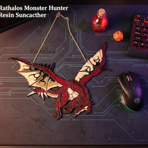 K&ouml;nnte beinhalten: Ein roter und beigefarbener Drachenanh&auml;nger mit goldener Kette, inspiriert von Rathalos Monster Hunter. Der Drache hat detaillierte Fl&uuml;gel und einen K&ouml;rper, mit dem Text "Rathalos Monster Hunter Resin Suncacther" in der oberen linken Ecke.