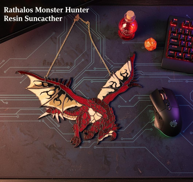 K&ouml;nnte beinhalten: Ein roter und beigefarbener Drachenanh&auml;nger mit goldener Kette, inspiriert von Rathalos Monster Hunter. Der Drache hat detaillierte Fl&uuml;gel und einen K&ouml;rper, mit dem Text "Rathalos Monster Hunter Resin Suncacther" in der oberen linken Ecke.