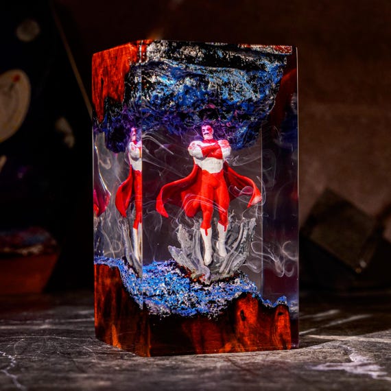 A handmade epoxy resin lamp where Omni-Man is literally embedded inside glowing light — part sculpture, part nightlight, all unhinged comic-book energy.