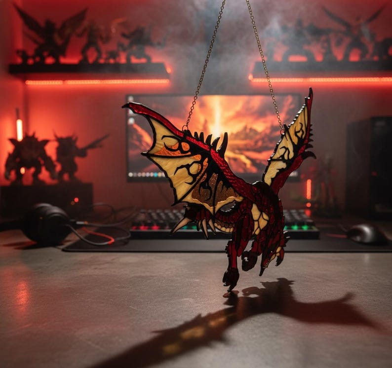 K&ouml;nnte beinhalten: Ein Drachenornament aus Buntglas, an einer Kette aufgeh&auml;ngt. Der Drache hat rote, gelbe und braune Farbt&ouml;ne mit detaillierten Fl&uuml;gelmustern. Das Ornament dient wahrscheinlich der Dekoration, m&ouml;glicherweise f&uuml;r einen Fantasy- oder Gaming-Enthusiasten.