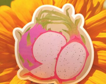 Könnte beinhalten: Ein Aufkleber mit einer aufgeschnittenen Drachenfrucht, die rosa Fruchtfleisch mit schwarzen Samen und eine rosa und grüne Schale zeigt. Der Aufkleber liegt auf einer leuchtend gelben Blume.