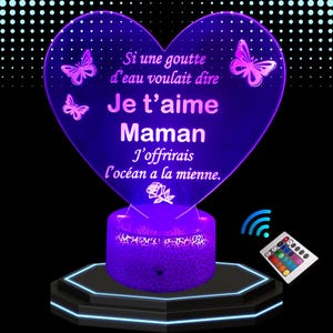 Peut inclure: Une veilleuse LED en forme de cœur de couleur violette avec le texte "Si une goutte d'eau voulait dire Je t'aime Maman J'offrirais l'océan a la mienne." La lumière est sur une base noire avec une télécommande.