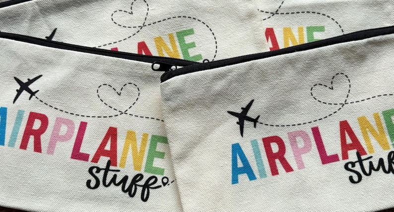 May include: Off-white canvas zipper pouches with black zippers. The pouches feature the words "AIRPLANE stuff" in colorful letters, with a dotted line and heart design. A black airplane graphic is also included.