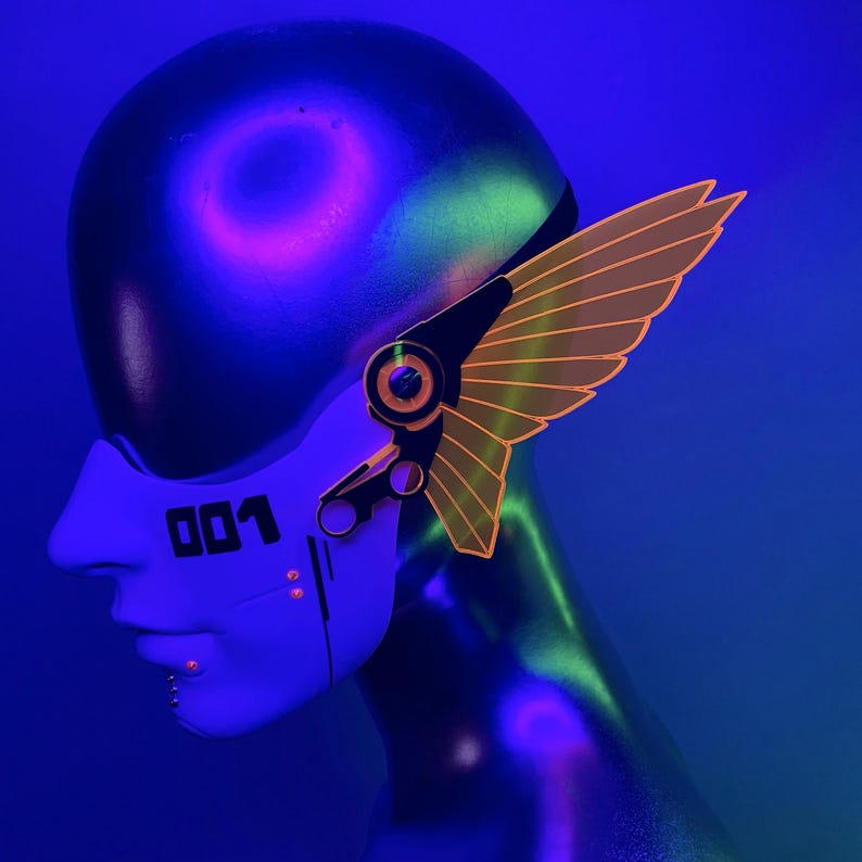 May include: A white face mask with the number "001" printed on it. The mask has a black and silver robotic design with a yellow and orange wing-shaped attachment on the side.