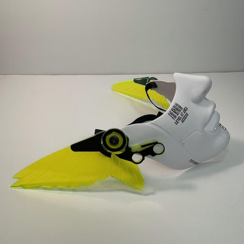 May include: White plastic mask with a human face design and two yellow wings. The mask has black and green accents and the text "ERROR 404" and "LEVEL 07 ACCESS" printed on the side.