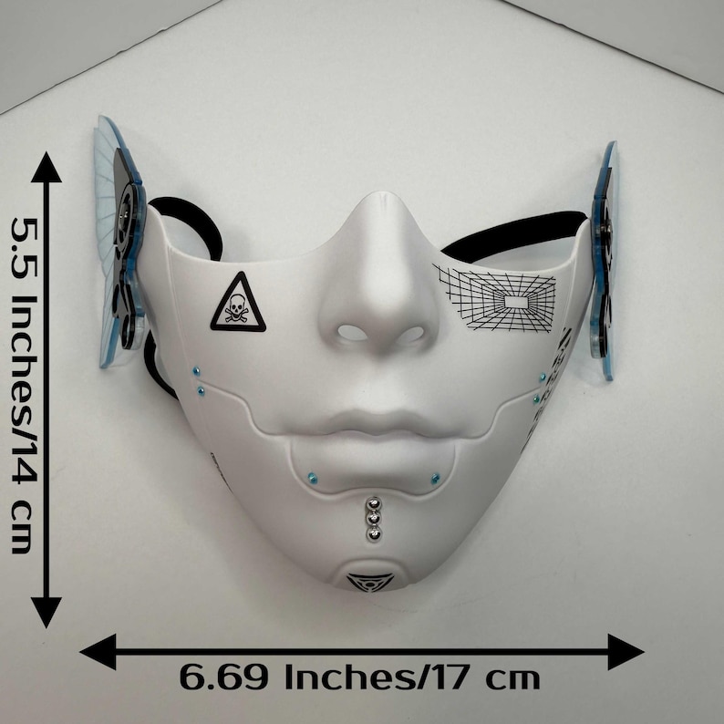 May include: White cybernetic mask with black accents, measuring 6.69 inches (17 cm) wide and 5.5 inches (14 cm) high. Features a skull and crossbones symbol, geometric designs, and blue embellishments. Includes black elastic straps.