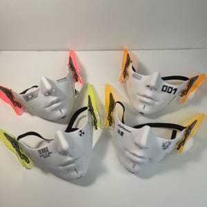 May include: Four white face masks with different designs and black straps. Each mask has a pair of colorful butterfly wings attached to the sides. The masks feature text such as "Cyberpunk", "001", and "Level 107 Area Access".