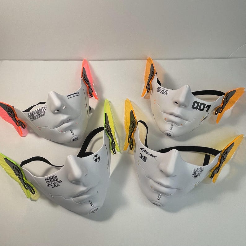 May include: Four white face masks with different designs and black straps. Each mask has a pair of colorful butterfly wings attached to the sides. The masks feature text such as "Cyberpunk", "001", and "Level 107 Area Access".